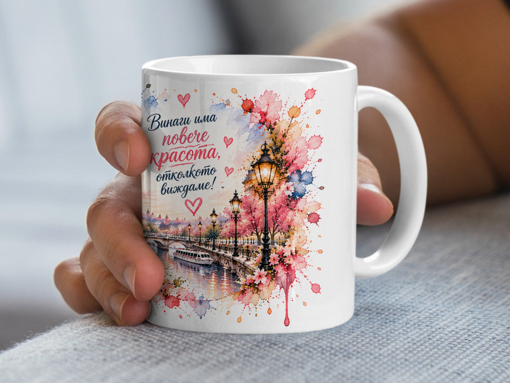 White mug with watercolor painting of a canal, bridge, boat, and blooming trees, with text.
